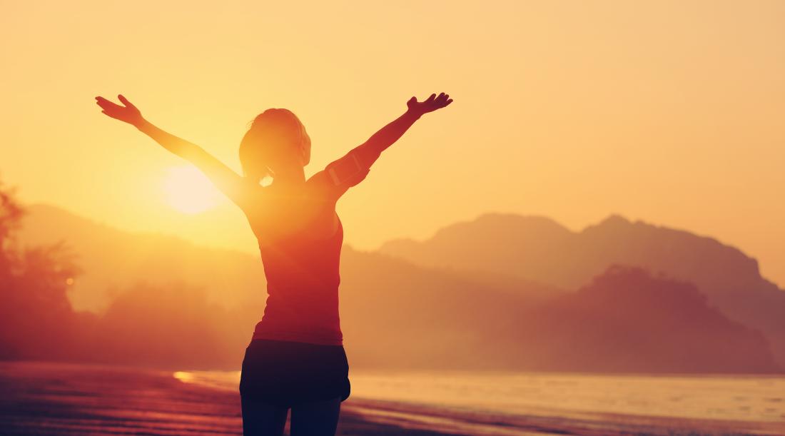 A happy woman raising her arms at sunrise, on a beach