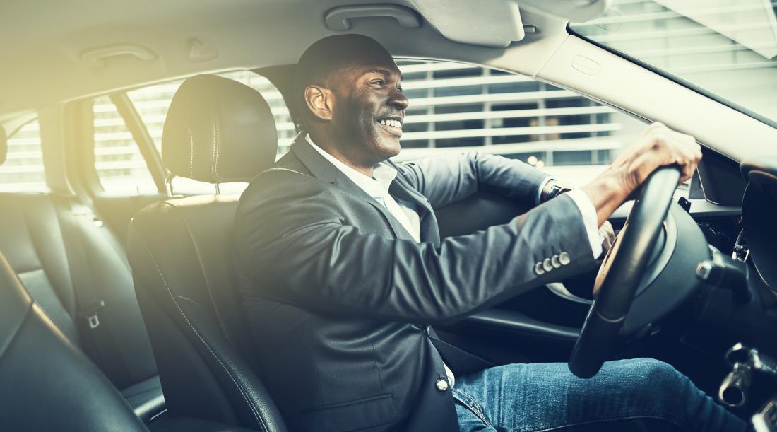 An African-American man smiling, driving to work.