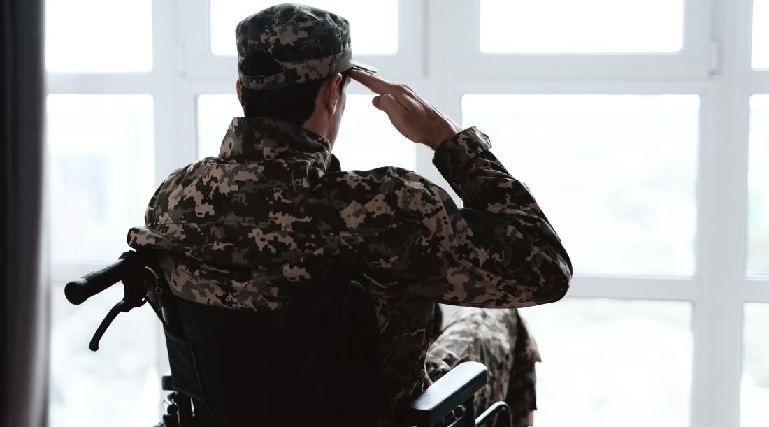 A man in a military uniform, sitting in a wheelchair saluting towards the window.