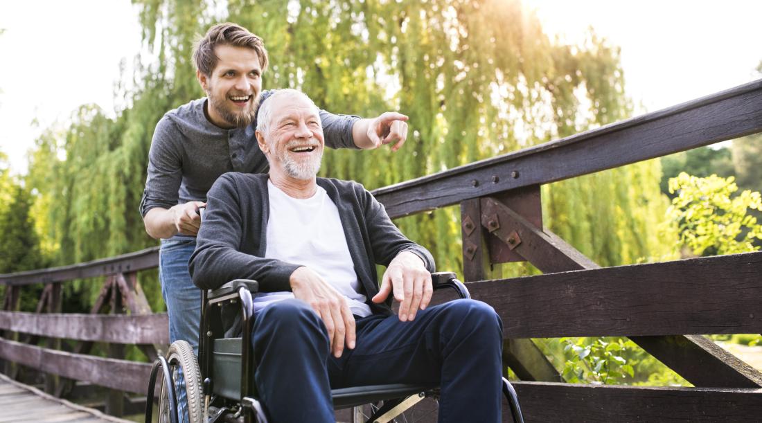 A young man pushing an elderly man in a wheelchair.
